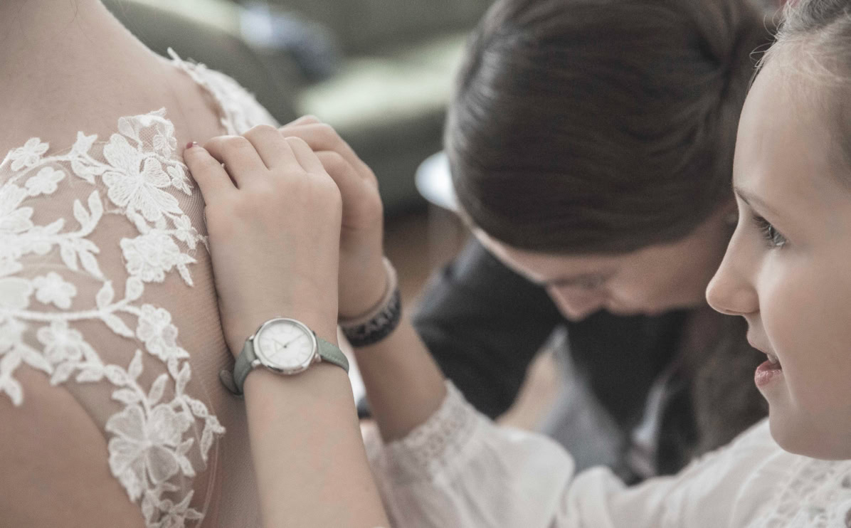 Personen helfen einer Frau, ein weißes Spitzenkleid zu schließen.