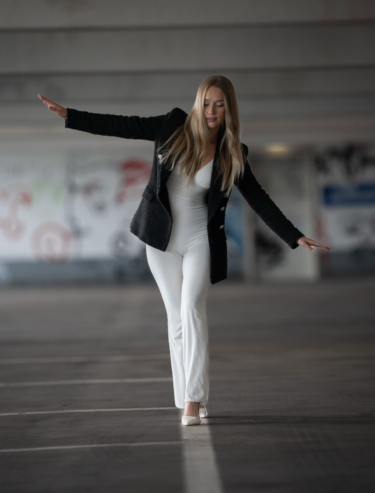 Eine Person in einem schwarzen Blazer und weißen Hosen balanciert auf einer Linie in einem Parkhaus.