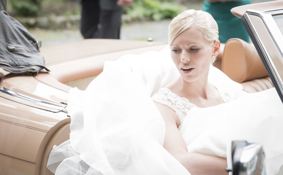 Frau in einem weißen Brautkleid sitzt in einem offenen Auto.