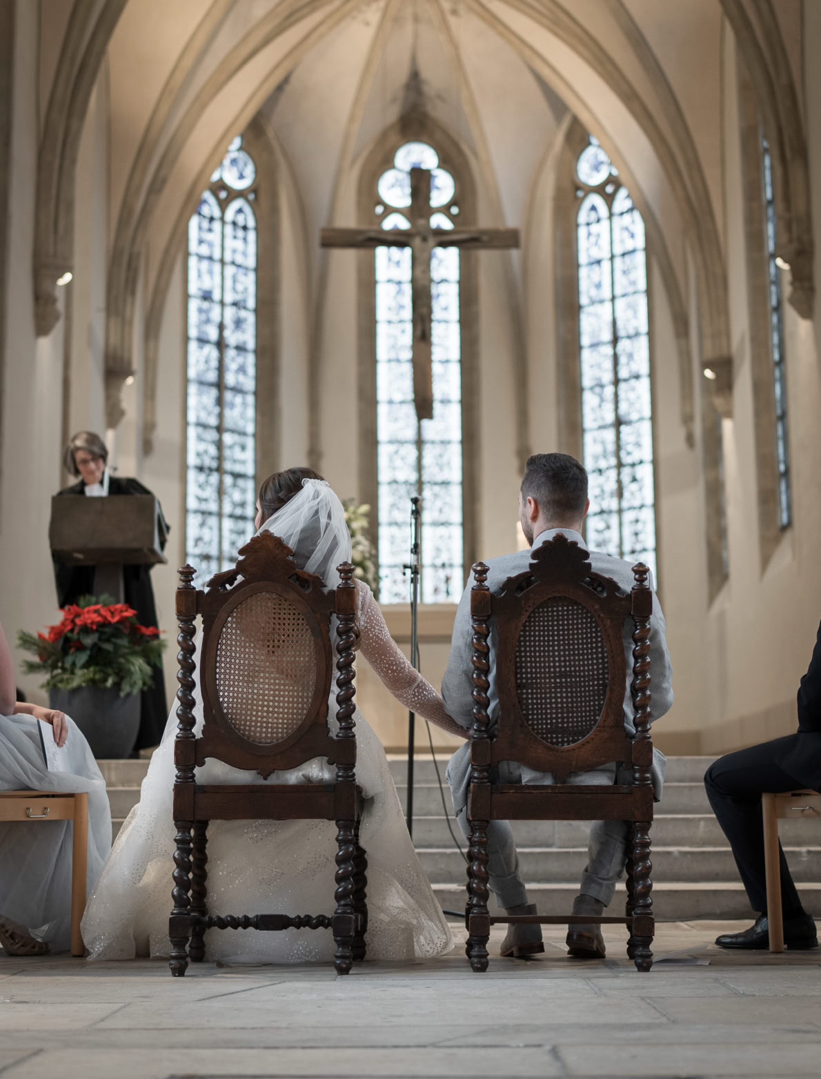 Ein Paar sitzt in einer Kirche vor einem Altar, umgeben von gotischen Fenstern und einem großen Kreuz.